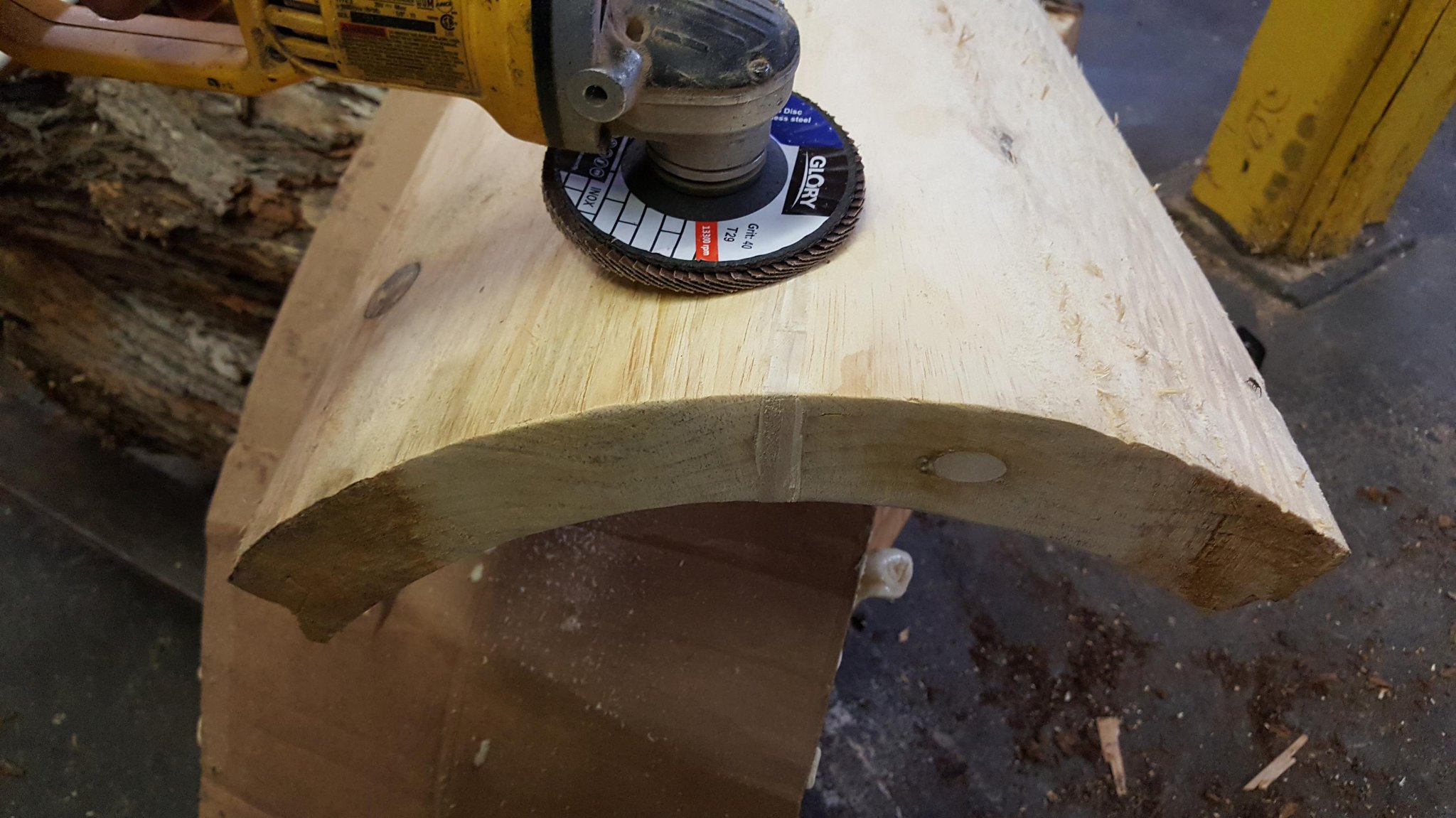 Angle grinder with a 40-grit flap disc smoothing the repaired crack surface on an IC WOOD hollow log — foam and wood surface being blended flush